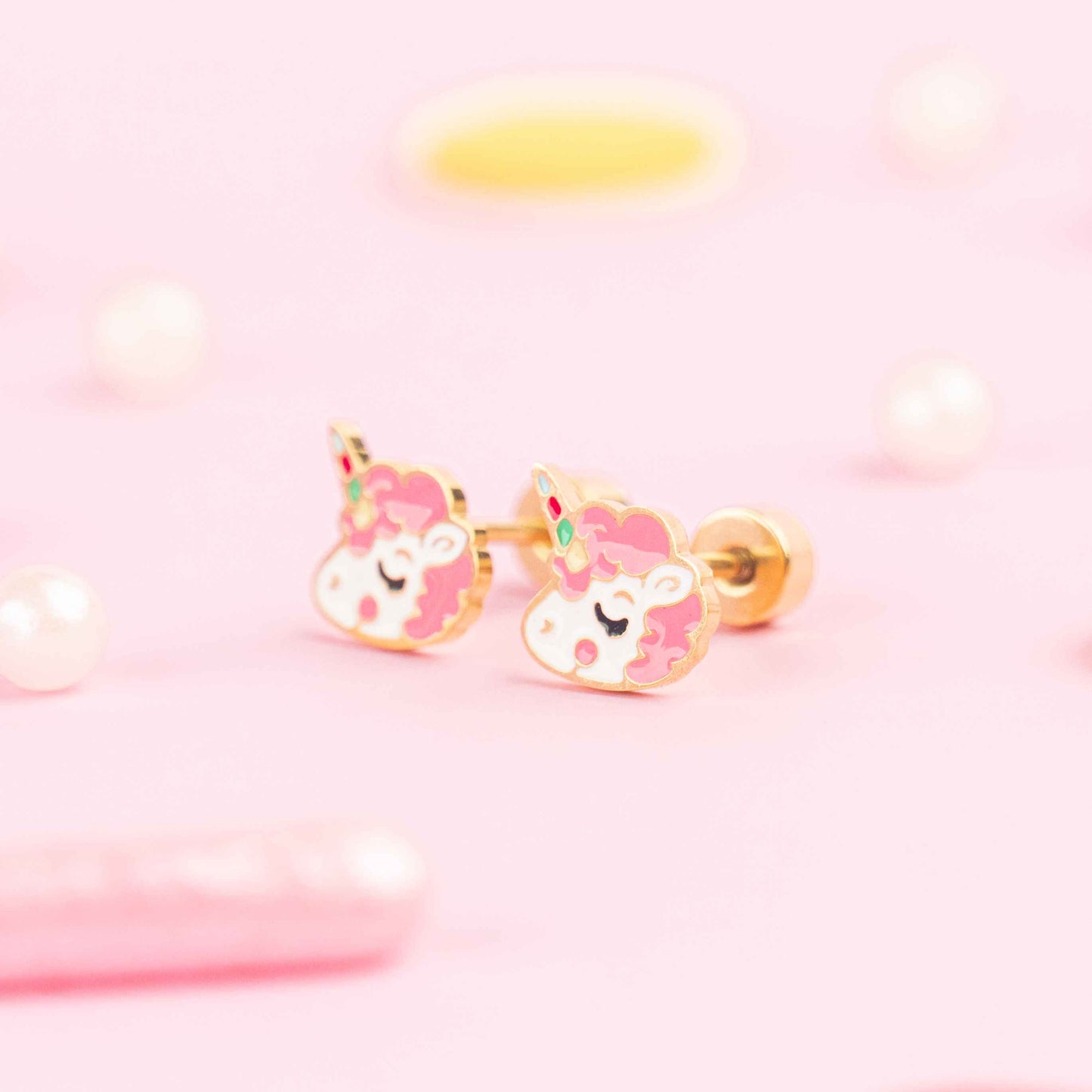 Unicorn-shaped earrings on a pink background